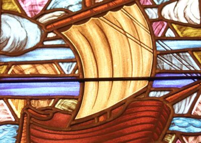 Stained glass artwork depicts a sailing ship navigating through waves with vibrant colors and intricate design details, evoking a sense of historical exploration.